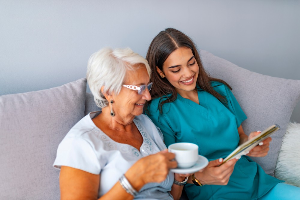 Senior woman drinking tea and reading with nurse