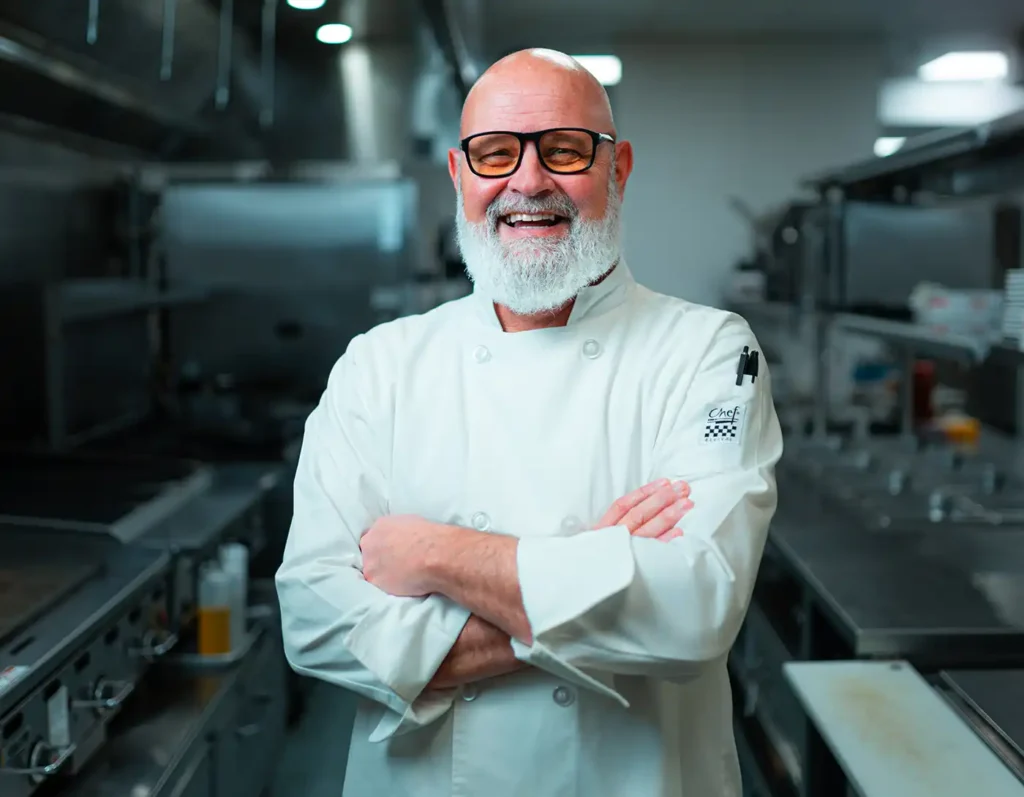 A chef stands smiling in a kitchen