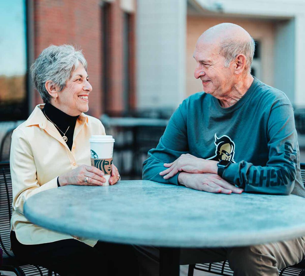 A senior couple talk over coffee at an outdoor table