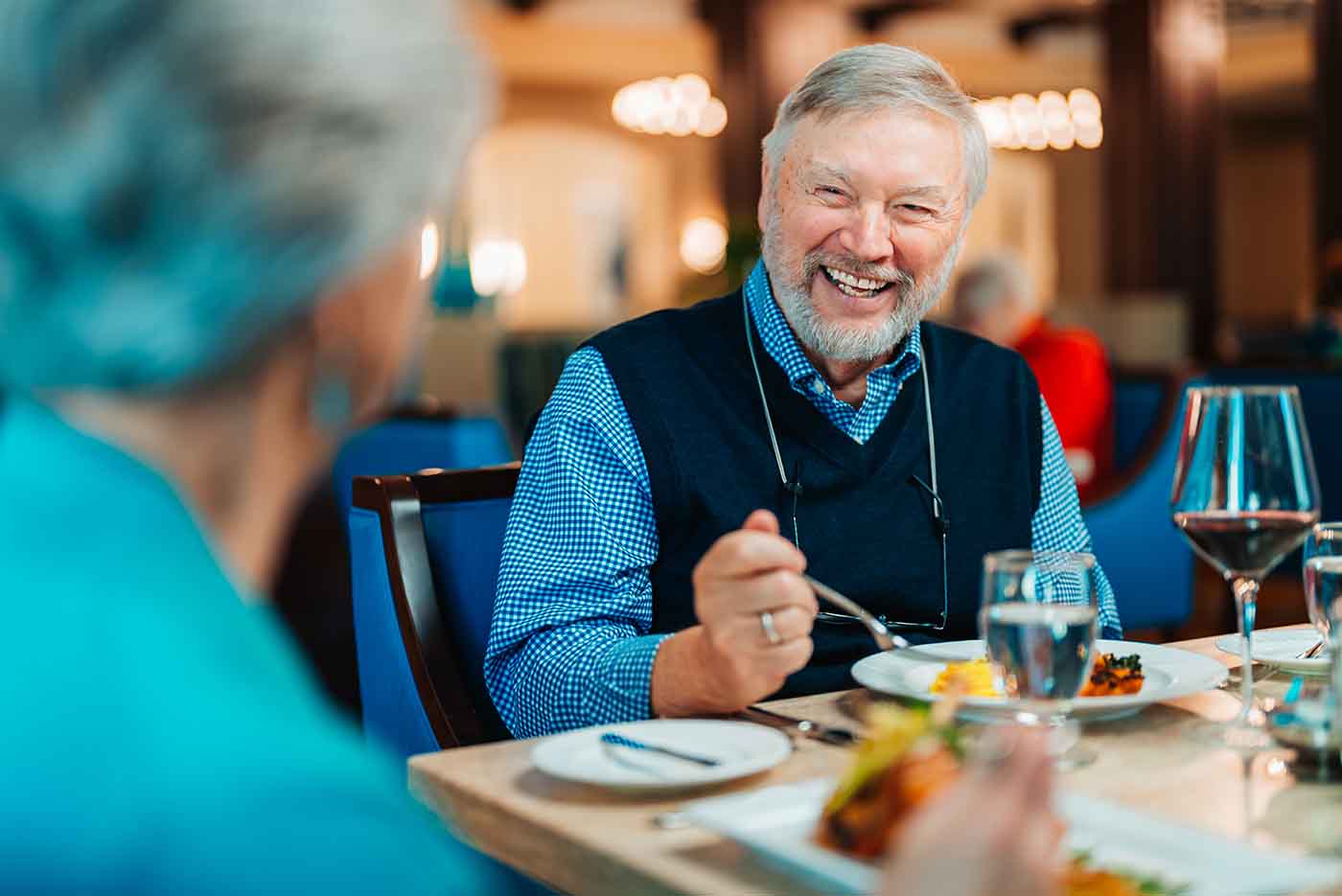 A senior man dines and laughs with a friend across a restaurant table
