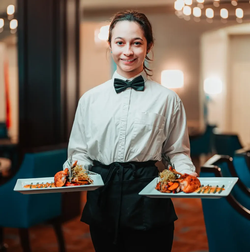 A server in black tie stands with two plates of expertly plated food