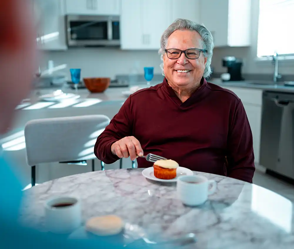 A senior man sits with a friend over coffee and dessert