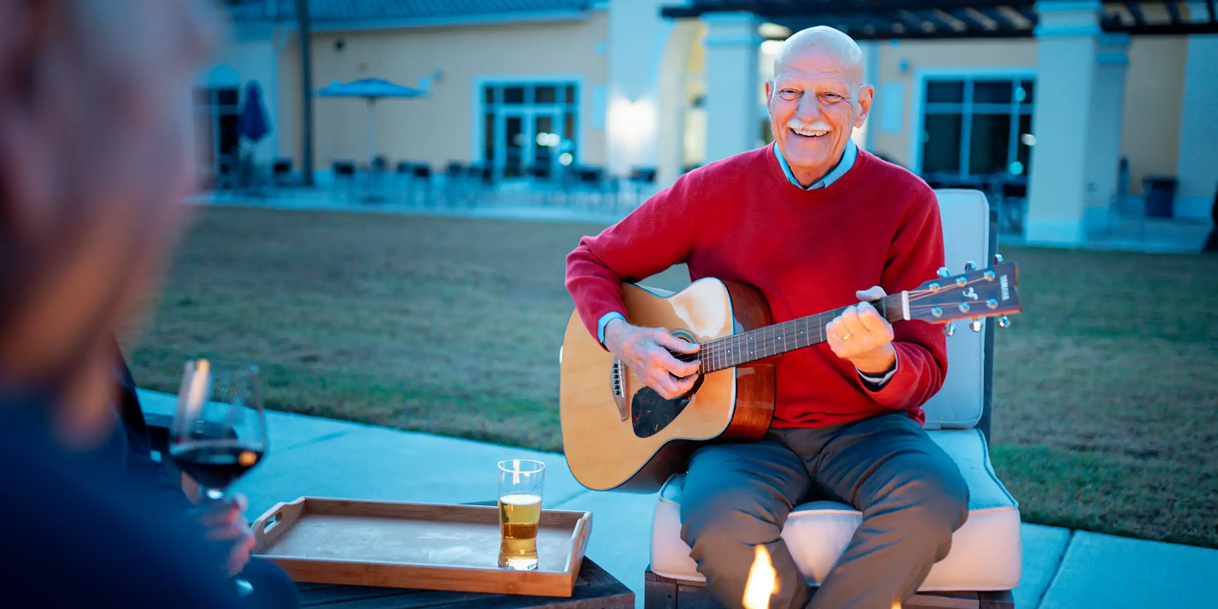 A senior man plays guitar fireside in a courtyard