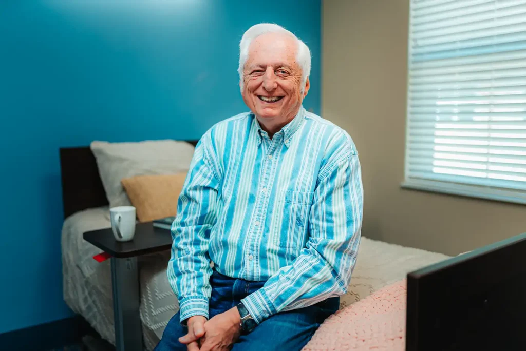 A senior man sits on the edge of a twin bed