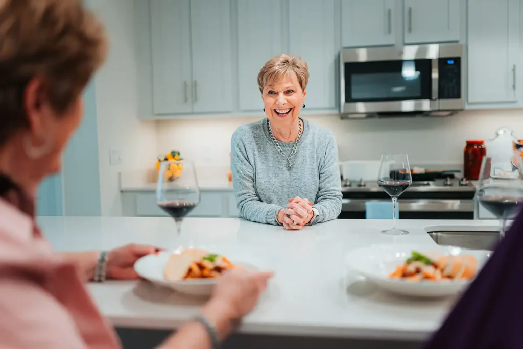 A senior woman serves food to friends on a modern kitchen island