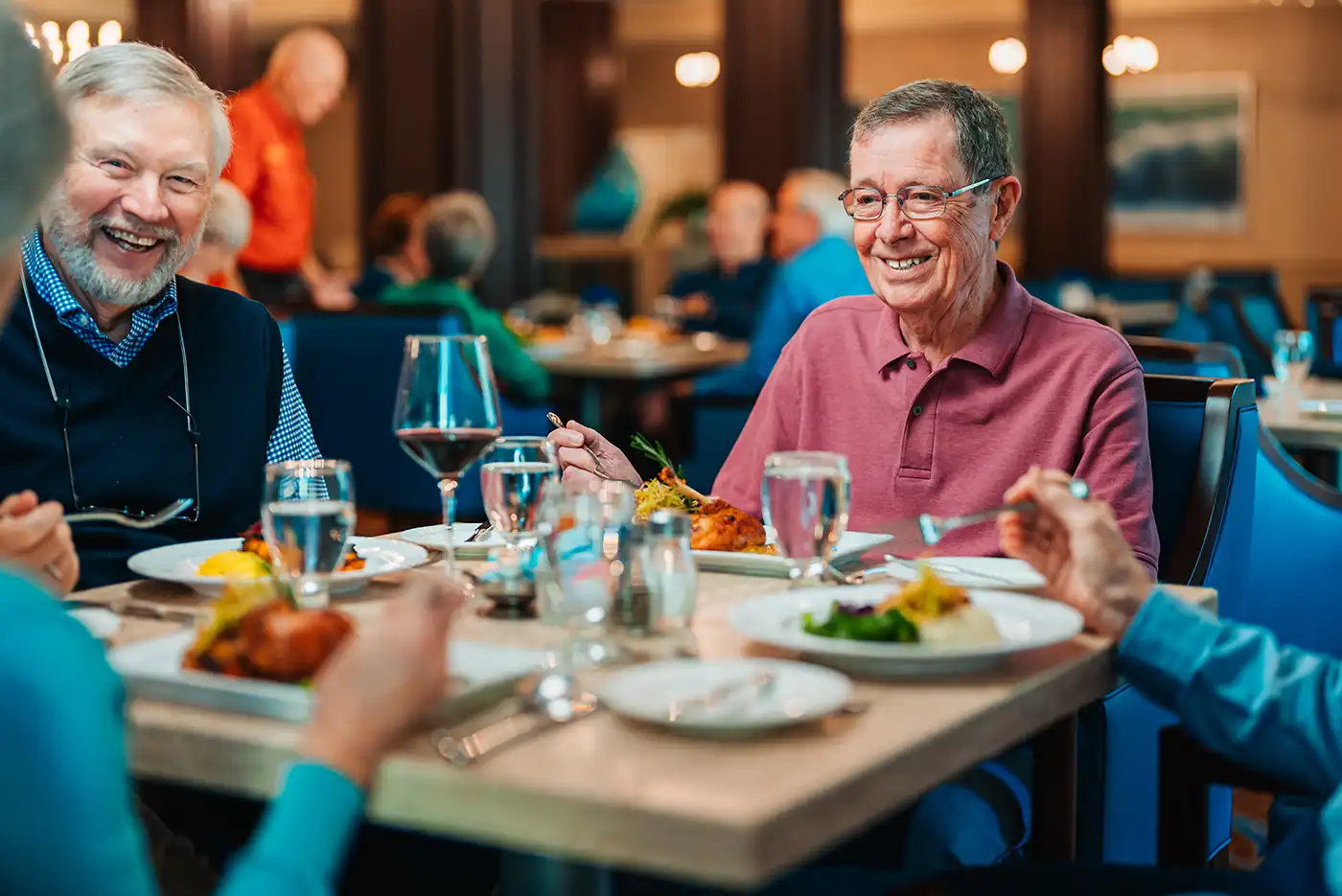 A senior sits with friends around a dining table in a restaurant setting