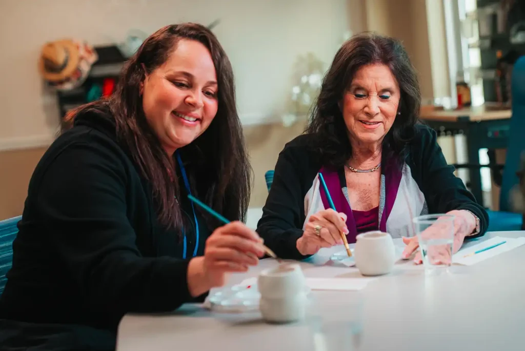 Two woman sit at a table and paint pottery